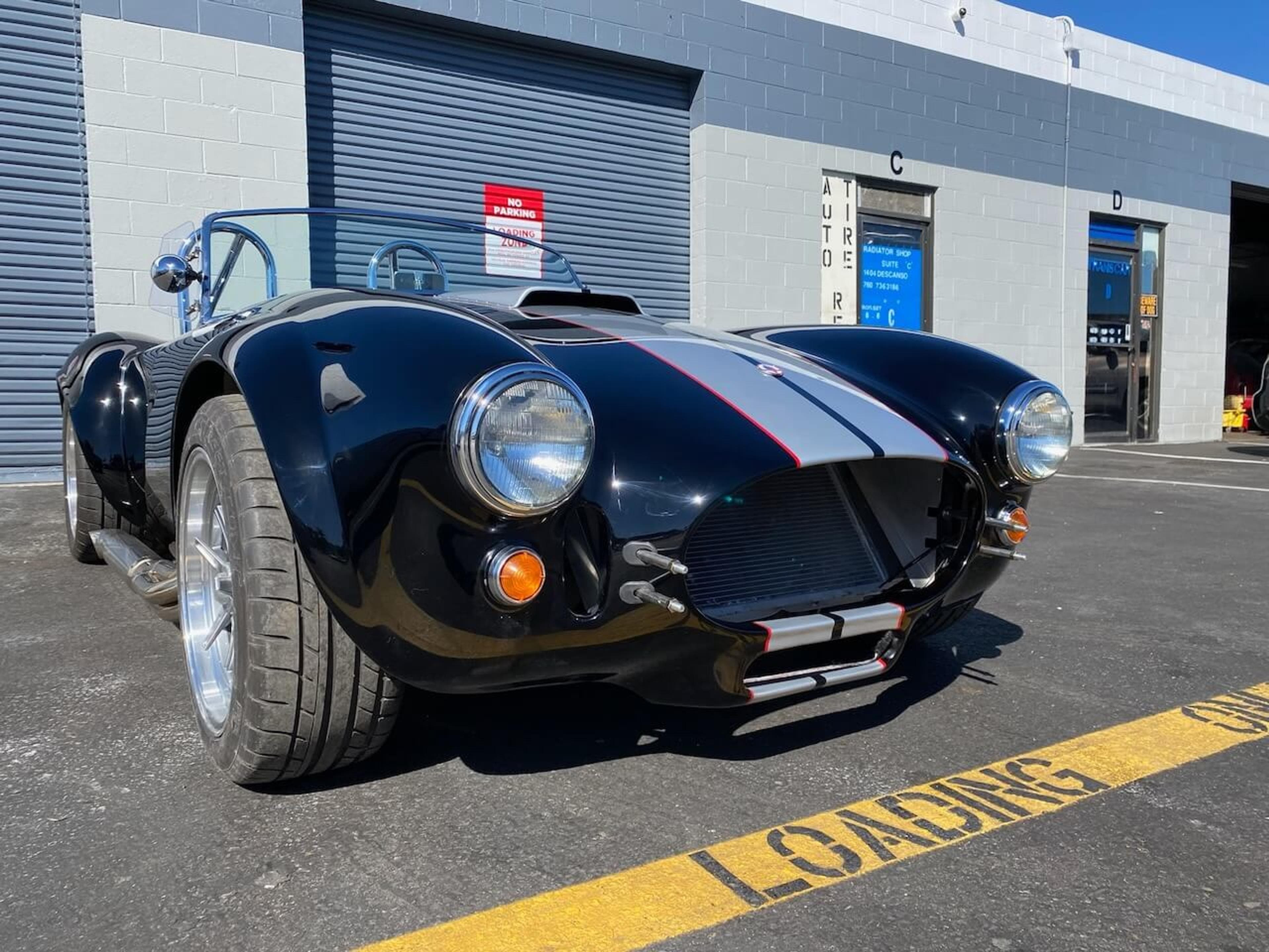Front three-quarter view of a black Shelby Cobra 427-style roadster after fiberglass body repair