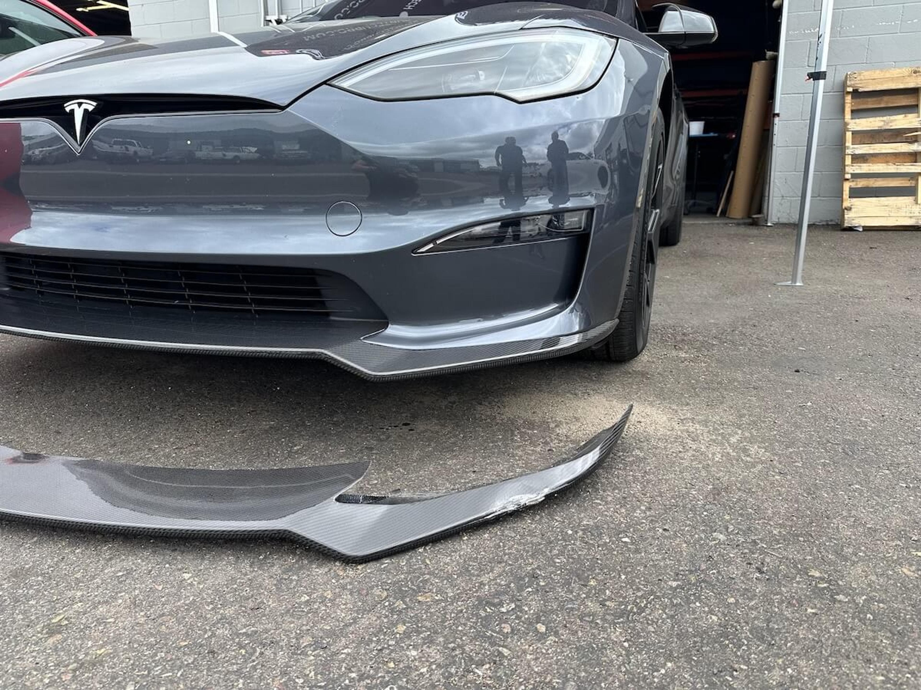 Tesla Model Y with damaged carbon fiber front lip removed and placed in front of the vehicle