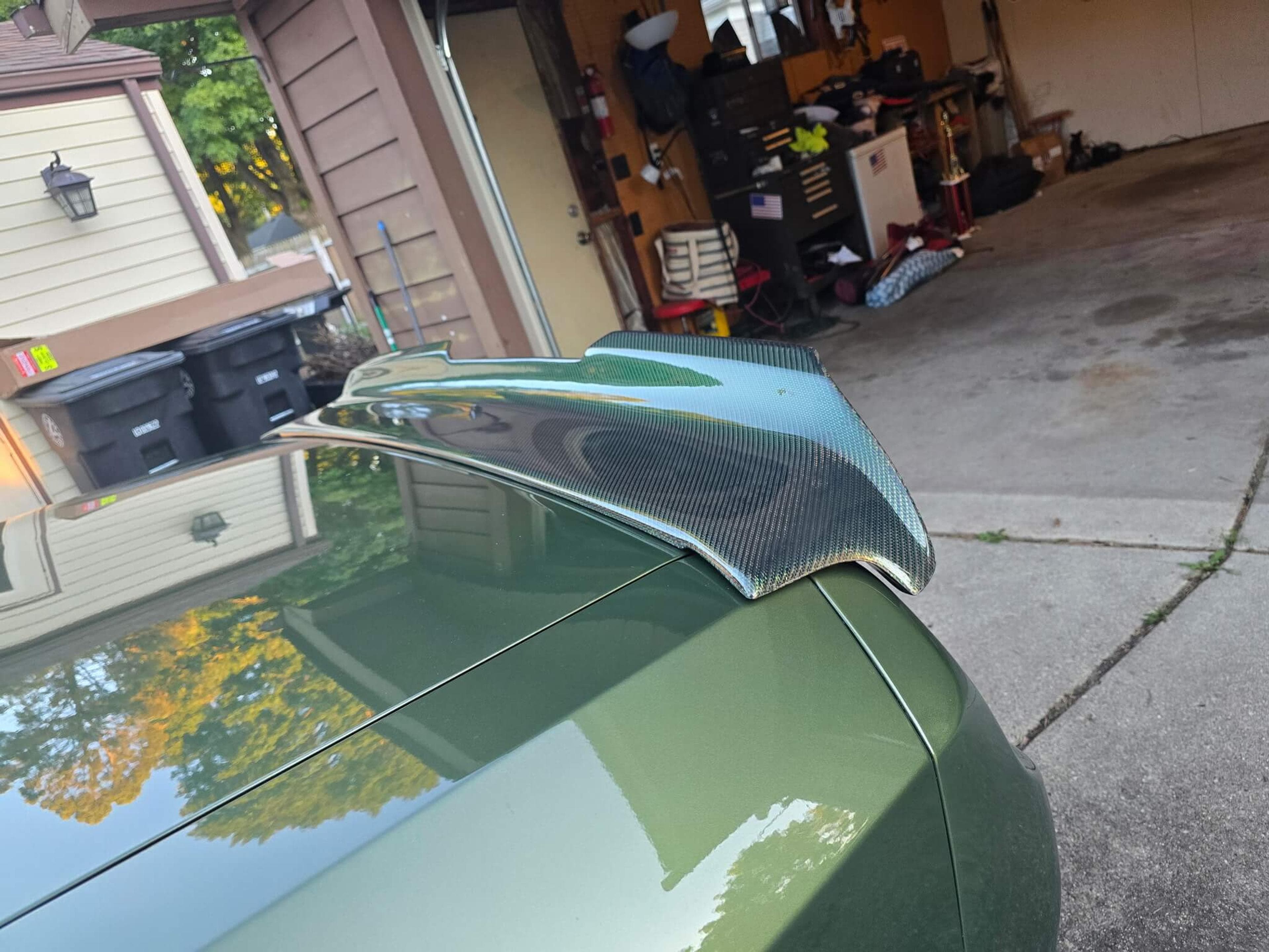 Rear-side view of a green Dodge Challenger showing its carbon fiber spoiler and matching fuel door.