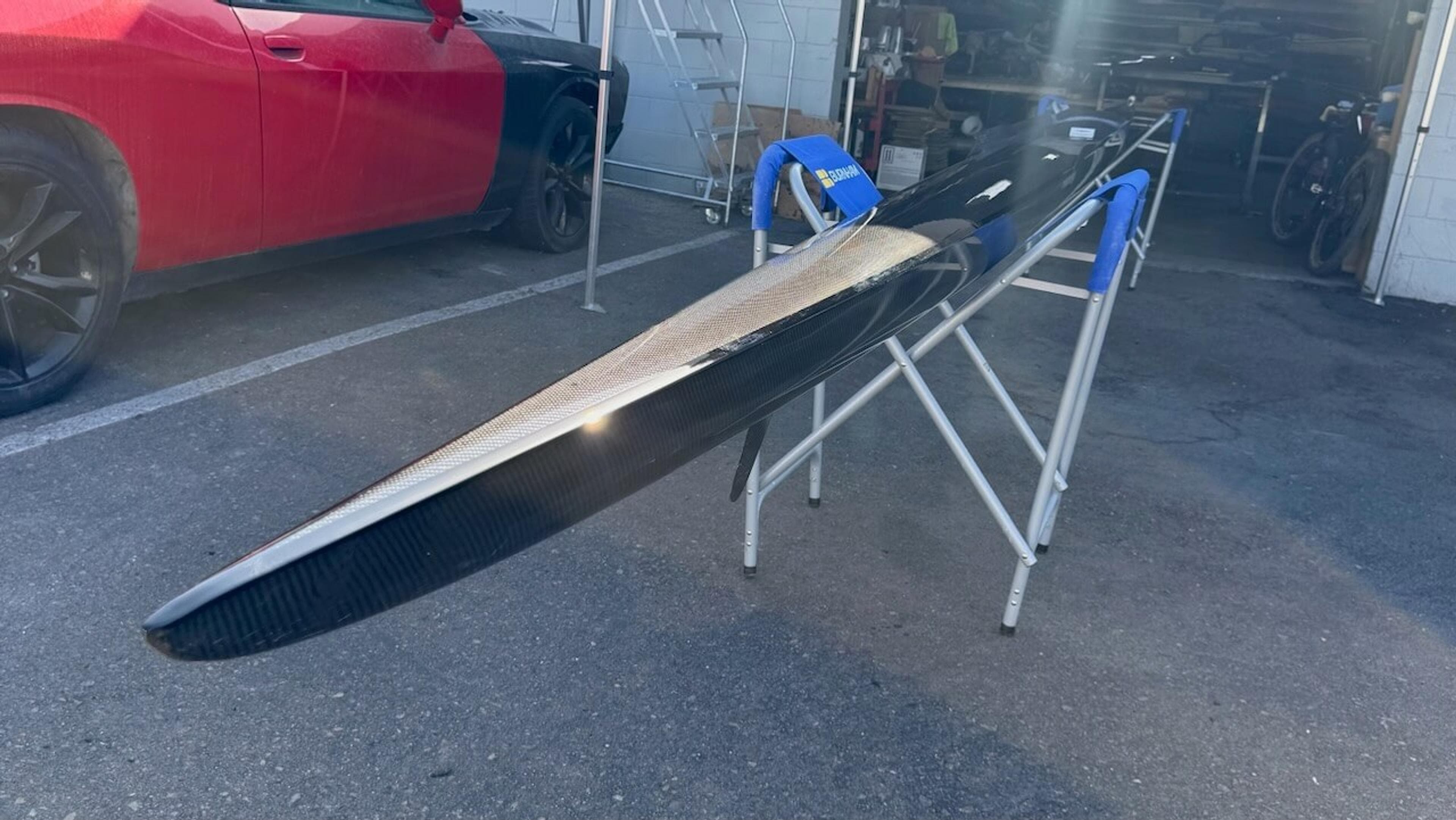 Fluidesign rowing shell supported on stands during carbon fiber repair and refinishing