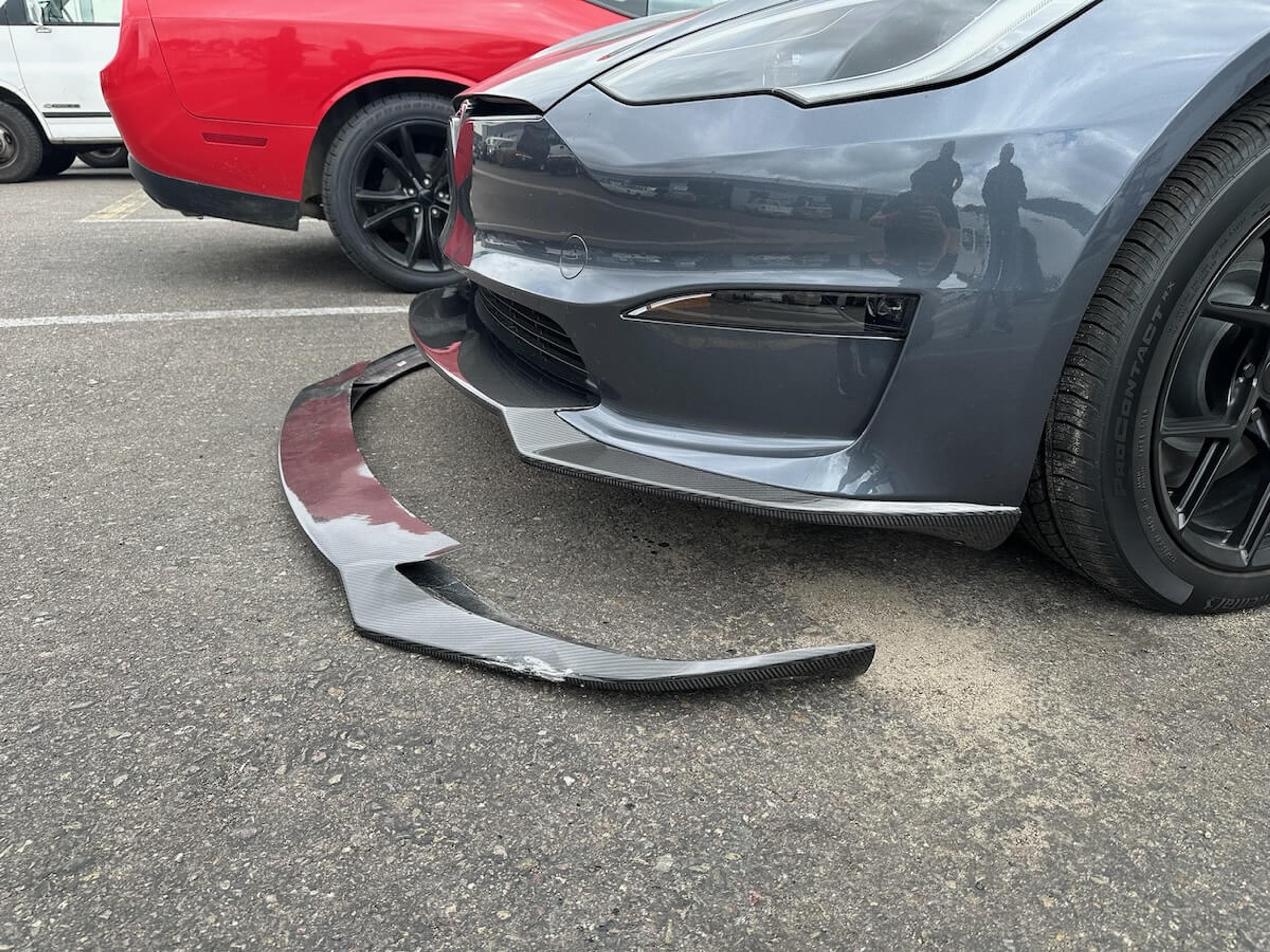Damaged carbon fiber front lip beside the front bumper of a gray Tesla Model Y