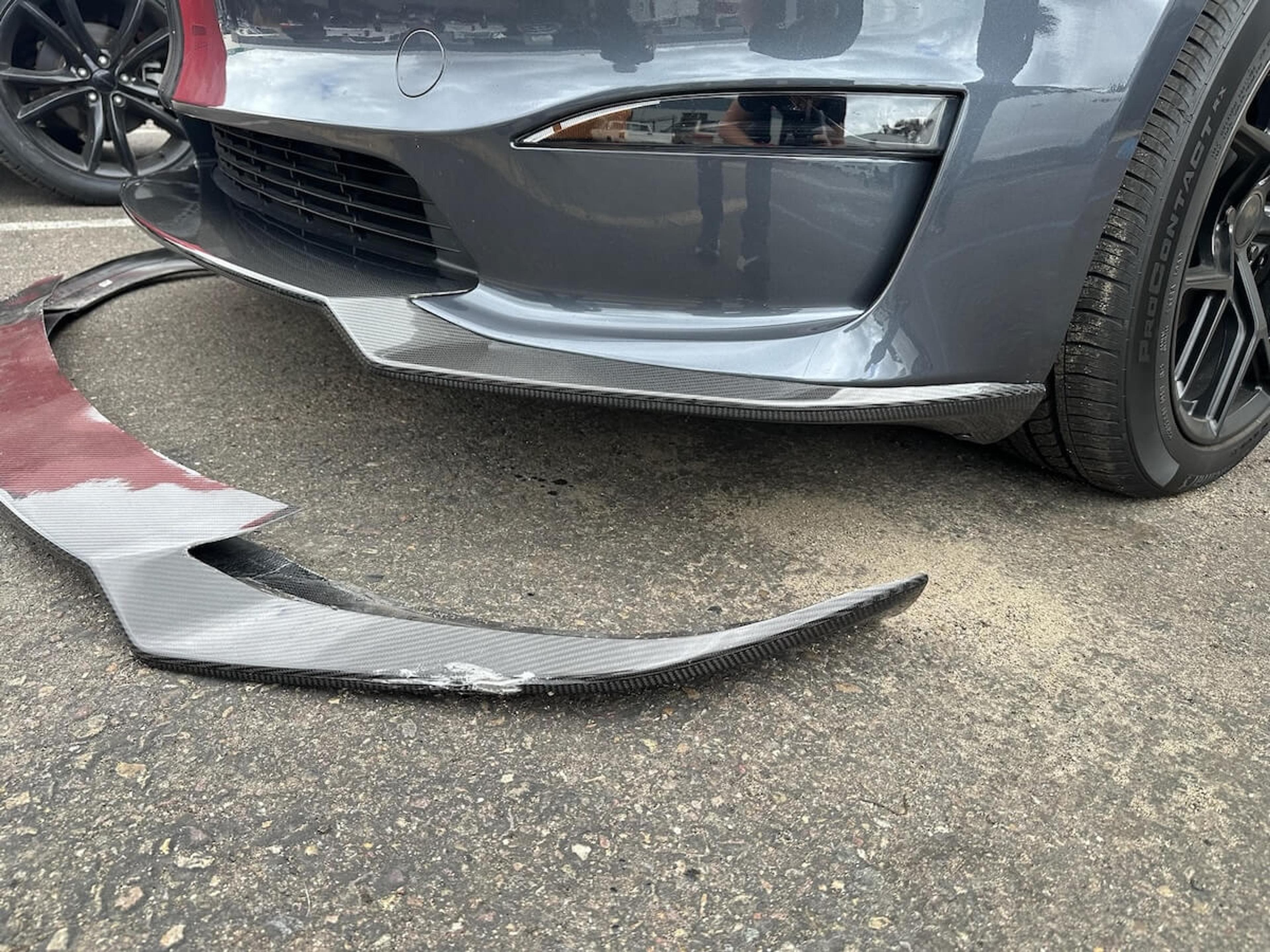 Close-up of damaged carbon fiber Tesla Model Y front lip next to the installed replacement