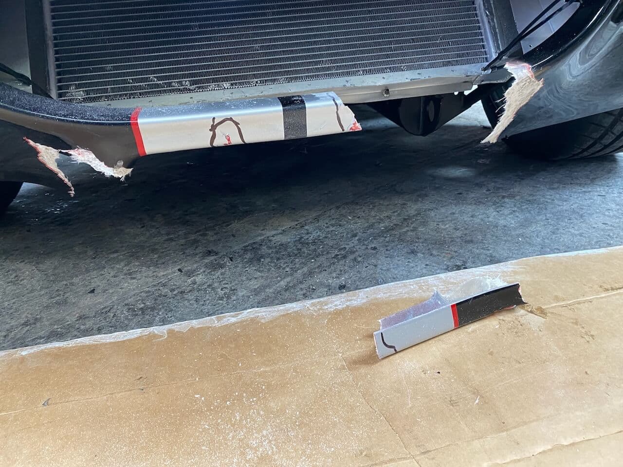 Close-up of cracked and broken fiberglass around the lower front opening of a Shelby Cobra-style roadster