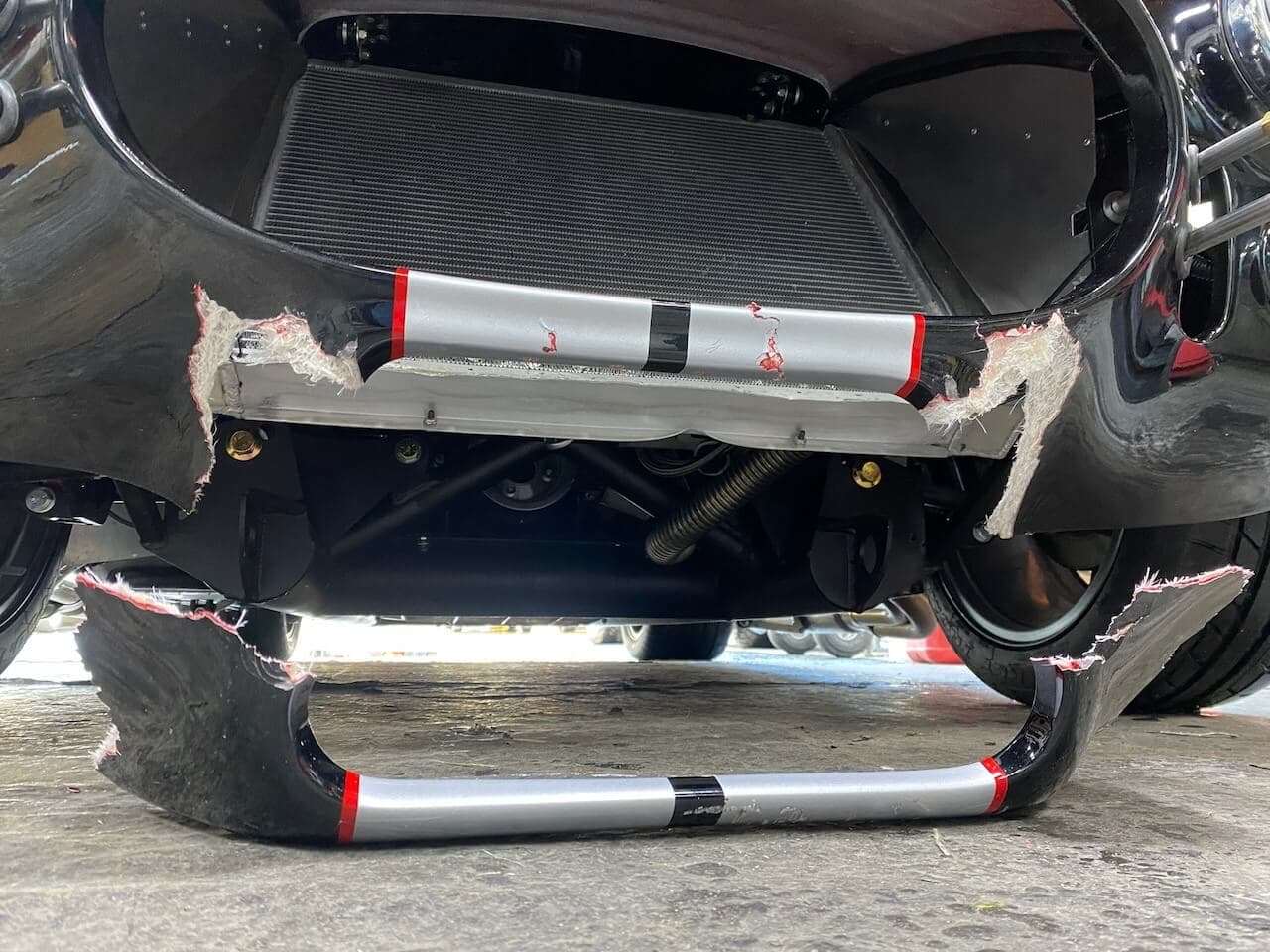 Front lower body section of a Shelby Cobra-style roadster with broken and torn fiberglass