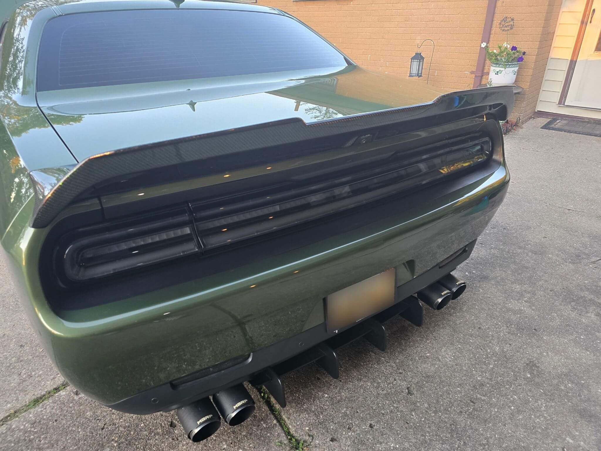 Rear view of a green Dodge Challenger with an installed carbon fiber trunk spoiler.