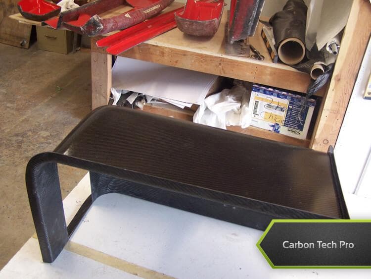 Custom-molded carbon fiber console structure crafted for high strength. Arch-shaped carbon fiber composite casing sitting on a workbench.